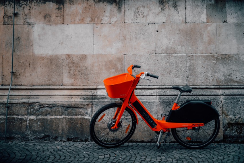 alt="Oranges E-Bike auf Ständer vor Gebäude"